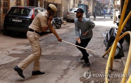 25일 인도 수도 뉴델리에서 경찰이 봉쇄령을 어긴 남성을 막대기로 때리는 장면. [로이터=연합뉴스]