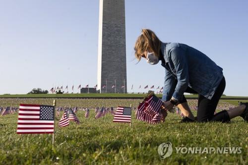22일(현지시간) 미국 워싱턴DC의 내셔널몰 워싱턴기념비에서 한 여성이 코로나19 사망자를 추모하기 위해 미국 국기를 꽂고 있다. [EPA=연합뉴스]