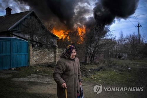포격으로 불 난 주택 앞에 서있는 우크라 주민