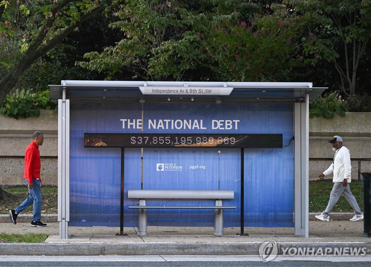 지난 7일(현지시간) 미국 국가 부채 규모 알림판이 부착된 미국 워싱턴 DC 버스 정류장 주변을 지나는 미국인들의 모습