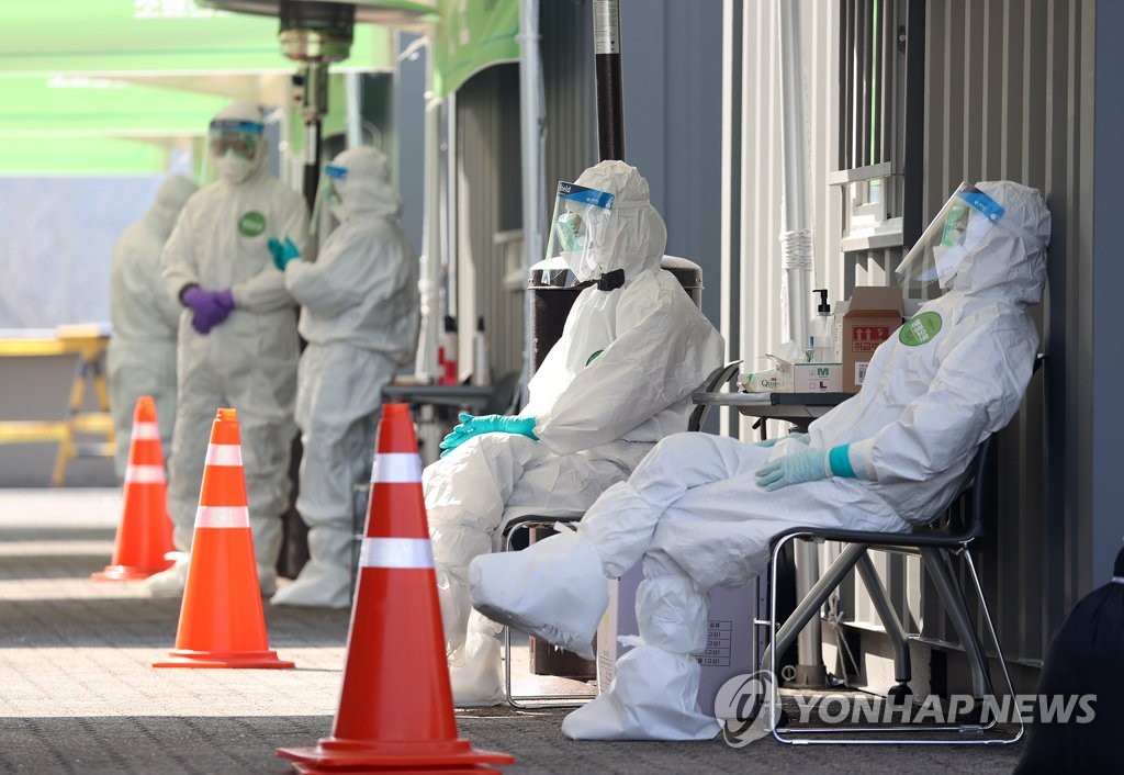 Medical workers wearing protective gear take a rest at a drive-through testing facility in Seoul on March 18, 2020. (Yonhap)