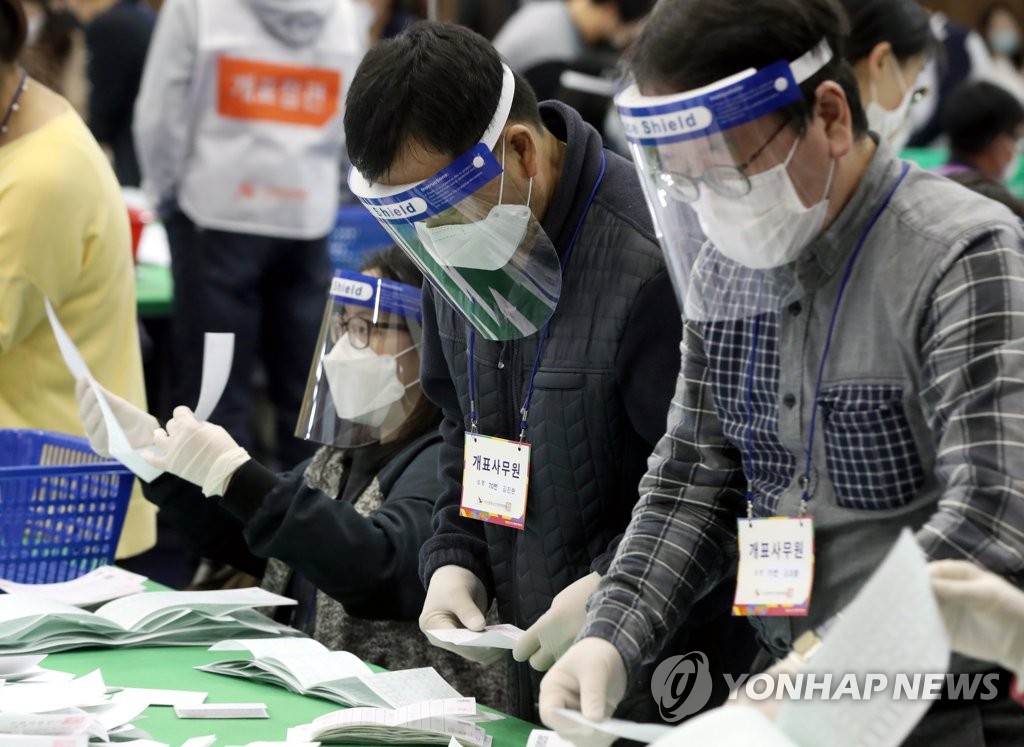 Officials wearing protective face guards, masks and plastic gloves go through ballots at a middle school stadium in the southern port city of Busan on April 15, 2020. (Yonhap)