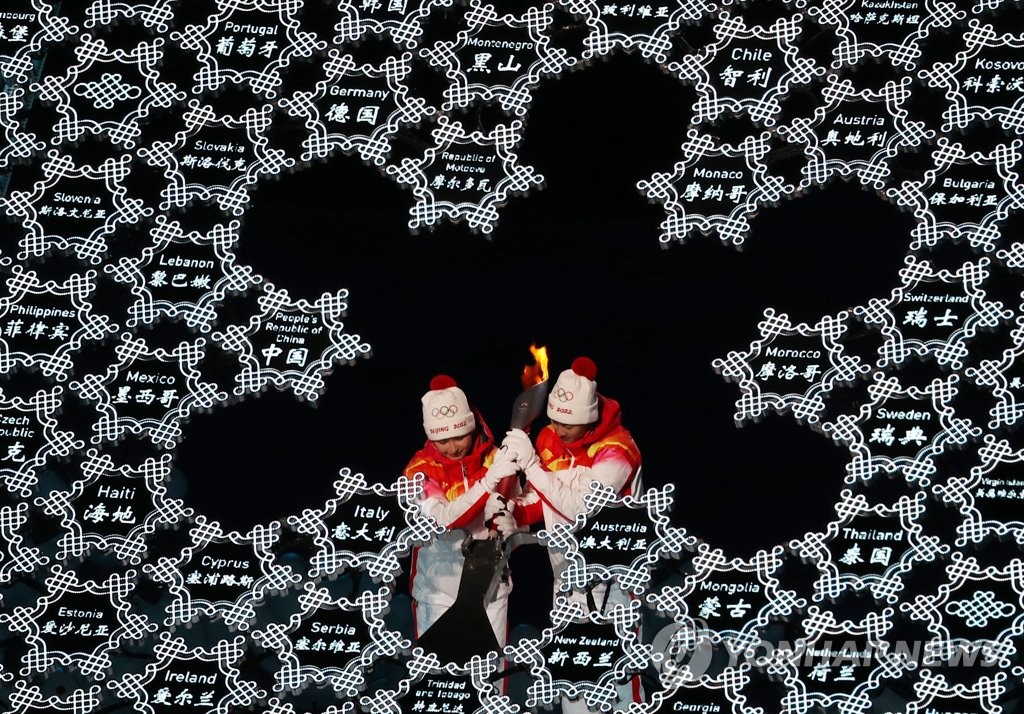 Dinigeer Yilamujiang and Zhao Jiawen, the last two torchbearers during the opening ceremony for the 2022 Beijing Winter Olympics, place the torch at the center of the snowflake-shaped cauldron at the National Stadium in Beijing on Feb. 4, 2022. (Yonhap)