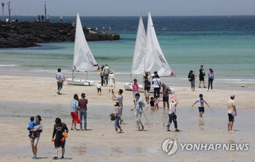 Tourists walk on a beach on the southern resort island of Jeju on May 7, 2017, the final day of a "golden holiday week" in South Korea. (Yonhap)