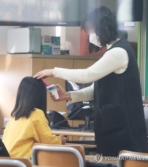 A pupil has her body temperature taken by a teacher during a day care program at an elementary school in Suwon, just south of Seoul, on March 2, 2020. (Yonhap)