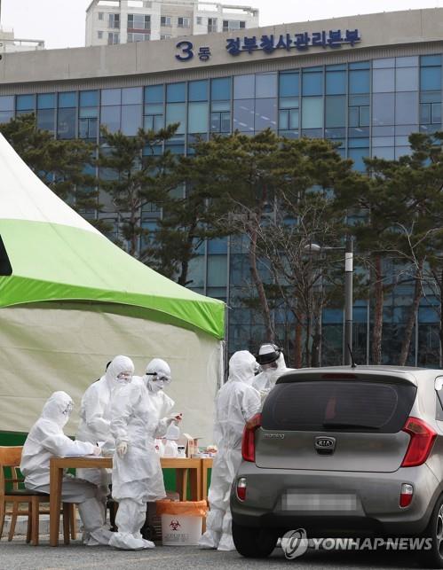 Medical workers wearing protective gear test a visitor at a drive-thru center for the new coronavirus at the government complex in Sejong, central South Korea, on March 13, 2020. At least 25 public officials in the city have been confirmed to be infected with the COVID-19 virus. (Yonhap)