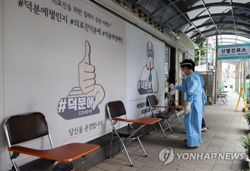 This undated file photo shows two people, wearing protective masks and a full gown, spraying disinfectants around chairs at a selected clinic for COVID-19. (Yonhap)
