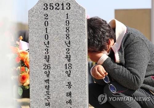 A bereaved family member of one of the 46 South Korean sailors killed in the torpedoing of the warship Cheonan by an infiltrating North Korean submarine within South Korean territorial waters in the West Sea on March 26, 2010, sheds tears in front of a grave at the National Cemetery in Daejeon, 164 kilometers south of Seoul, on March 25, 2021, one day ahead of the incident's anniversary. (Yonhap)