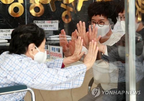 A mother (L) greets her daughters, with a glass wall between them, at a nursing hospital in Busan, on May 7, 2021, one day ahead of Parents' Day amid the pandemic. (Yonhap)
