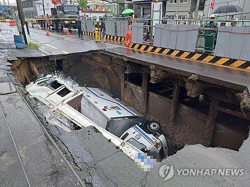 En esta fotografía proporcionada por las autoridades de bomberos, los camiones permanecen volcados dentro de un socavón en una carretera de la ciudad de Busan, en el sureste del país, el 21 de septiembre de 2024, tras fuertes lluvias. (FOTO NO A LA VENTA) (Yonhap)