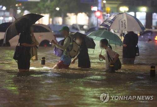 La gente camina por una carretera inundada, en el sur de Seúl, el 8 de agosto de 2022 por la noche, mientras la lluvia más intensa en 80 años, de más de 100 milímetros por hora, azotaba Seúl y sus alrededores.