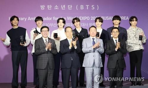 La foto de archivo muestra al primer ministro surcoreano, Han Duck-soo (segundo por la izda., primera fila), posando para una foto con la sensación del K-pop BTS (segunda fila), y el presidente del Grupo SK, Chey Tae-won (segundo por la dcha., primera fila), durante una ceremonia para nombrar al septeto del K-pop como embajador promocional para albergar la Expo Mundial 2030 en la ciudad portuaria sureña de Busan, el 19 de julio de 2022, en Hybe, en Seúl.