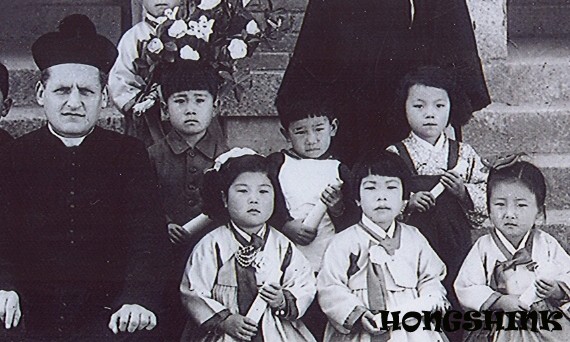 Kim Hong-shin at the kindergarten graduation ceremony (boy in the middle of the back row, French priest on the far left)