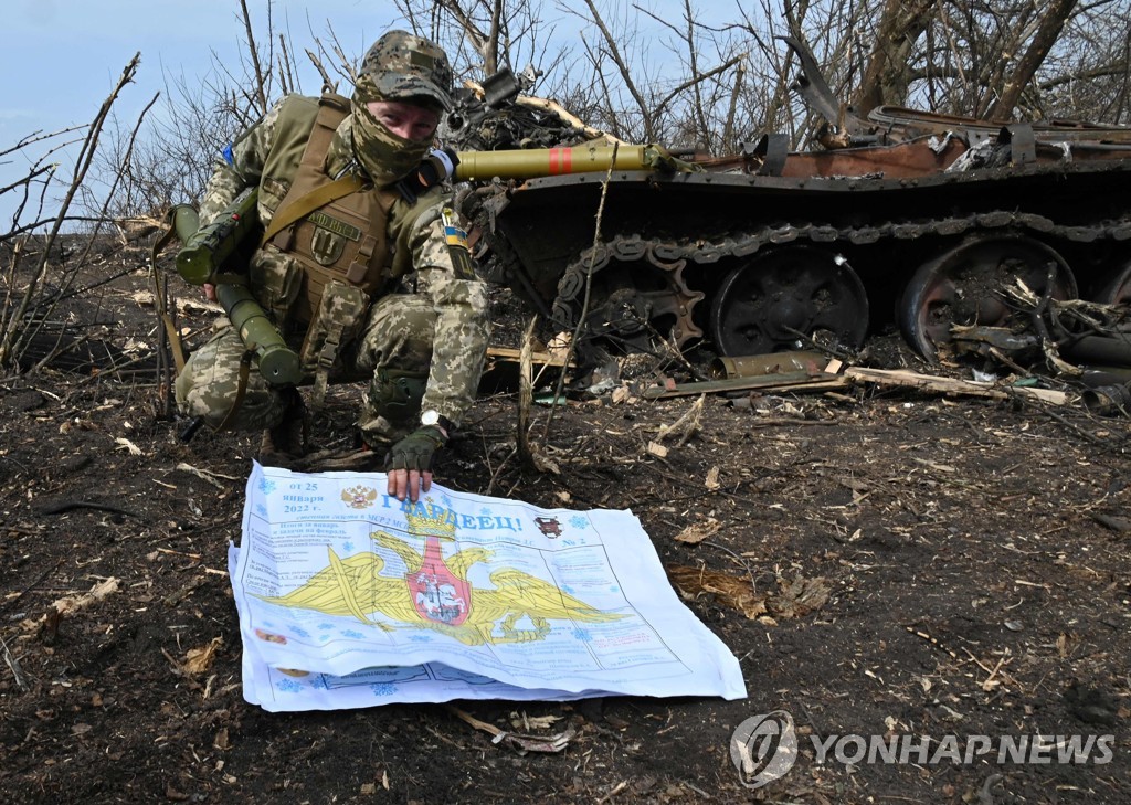 파괴된 러시아 탱크 앞에서 러시아군 서류를 펴는 우크라이나 병사