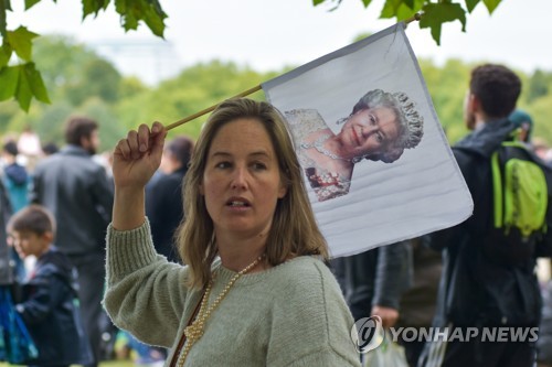 엘리자베스 2세 여왕의 장례식이 열린 19일 런던 시내 그린 파크에서 한 여성이 여왕의 초상화가 그려진 깃발을 들고 있다.