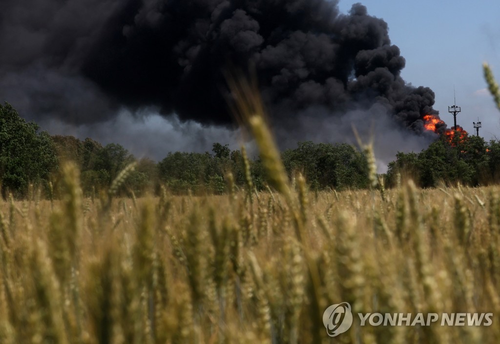우크라이나 밀밭 뒤로 가스 처리공장이 폭격받아 불타오르고 있다.