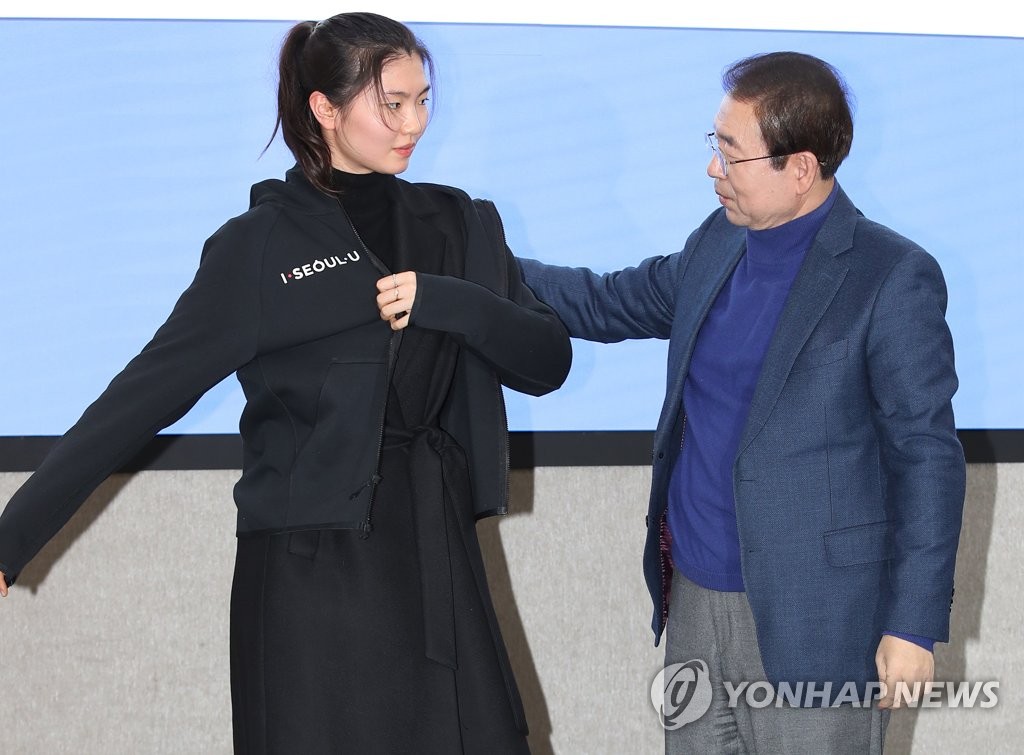 South Korean short track speed skater Shim Suk-hee (L) puts on a jacket for the Seoul City Hall semi-pro club, with the help of Seoul Mayor Park Won-soon, during a ceremony at the city hall building in central Seoul on Jan. 3, 2020. (Yonhap)