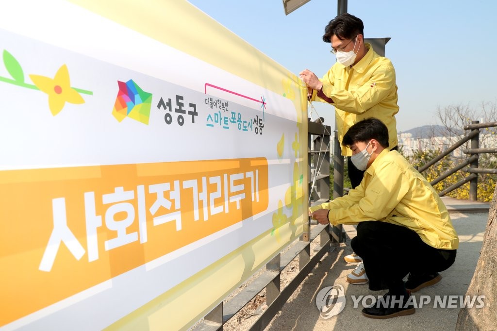 This photo, provided by the office of Seongdong Ward in Seoul on March 25, 2020, shows officials setting up a placard that detailed the cancellation of a forsythia festival and called for social distancing. (PHOTO NOT FOR SALE) (Yonhap)