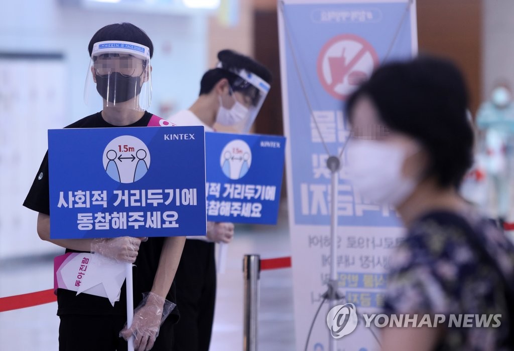 Workers at a construction expo hold signs asking visitors to follow social distancing measures at KINTEX exhibition hall in Goyang, north of Seoul, on Aug. 20, 2020. (Yonhap)