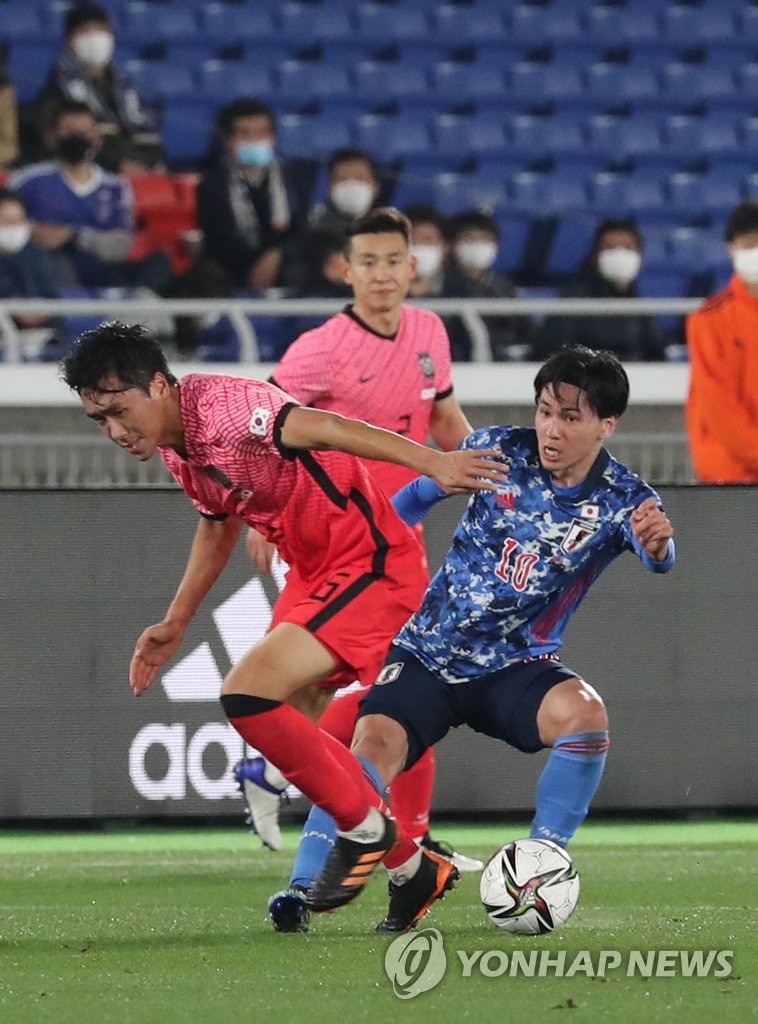 Won Du-jae of South Korea (L) battles Takumi Minamino of Japan for the ball during their friendly football match at Nissan Stadium in Yokohama, Japan, on March 25, 2021. (Yonhap)
