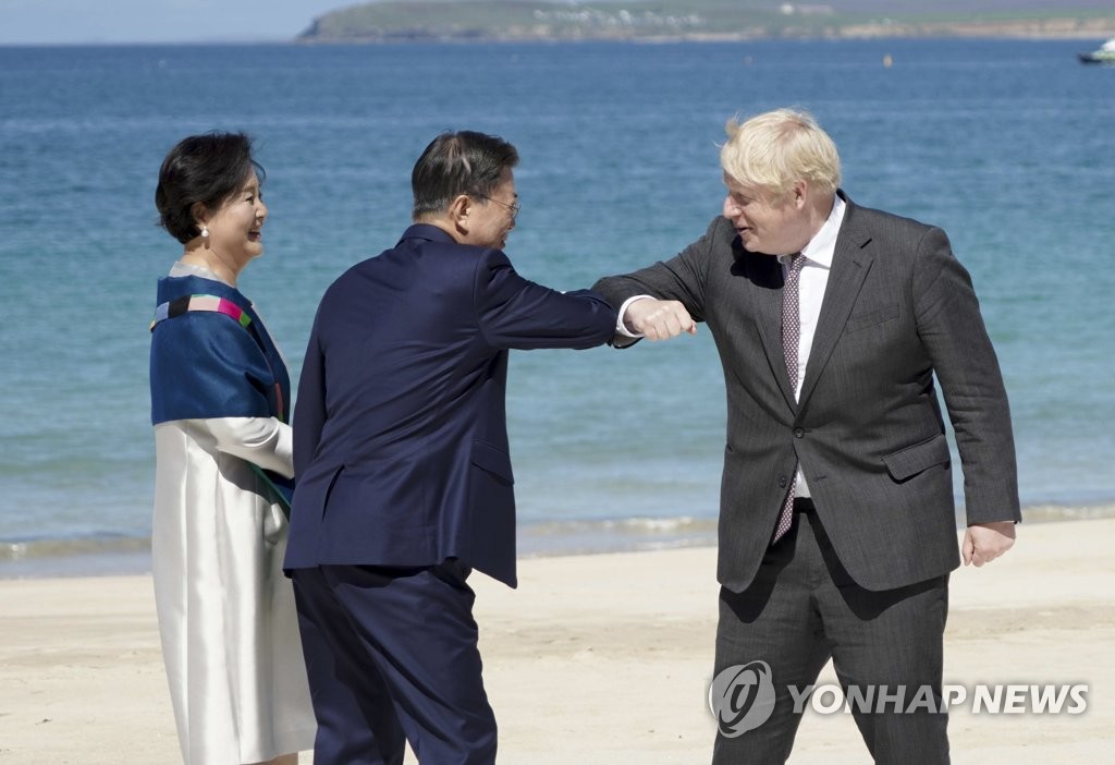 Le président Moon Jae-in (au centre) salue du coude le Premier ministre britannique Boris Johnson (à dr.) le samedi 12 juin 2021 lors d'une réception sur une plage de Carbis Bay en Cornouailles, au Royaume-Uni.