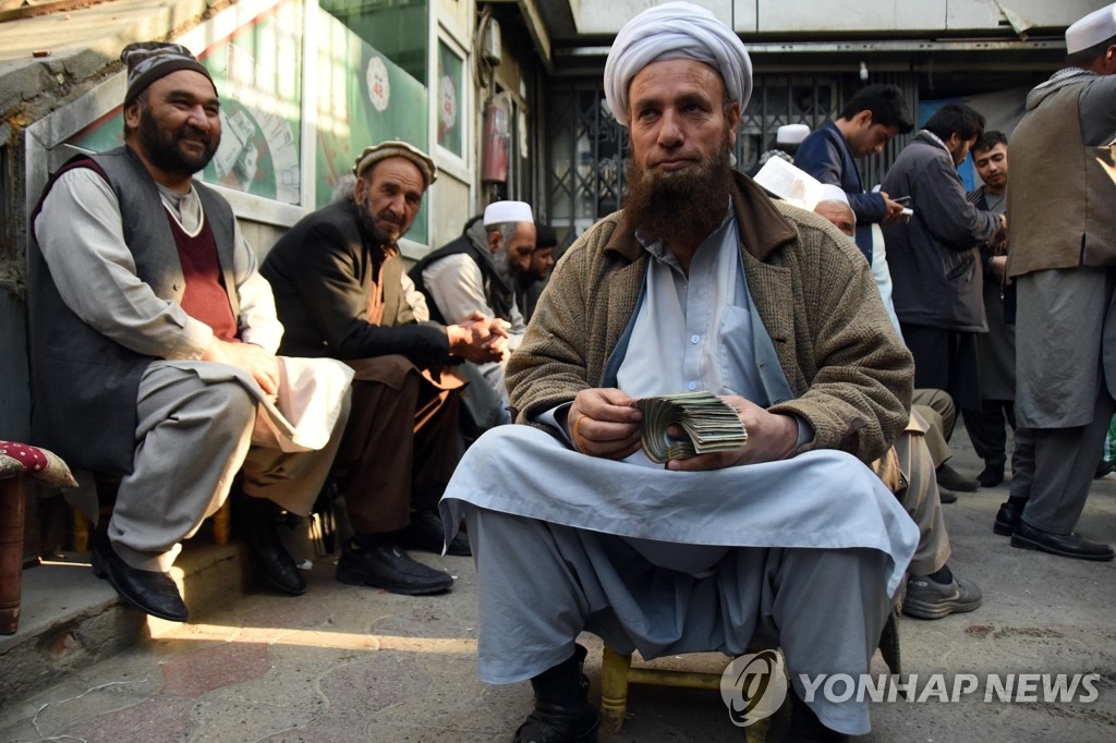 アフガニスタンの首都カブールの闇市で紙幣を数える両替商。同地では通貨アフガニの対ドルでの下落が続いている＝２７日、カブール（聯合ニュース）