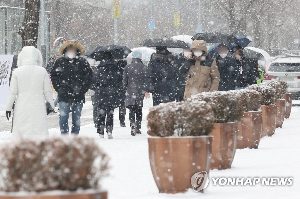 Las personas caminan sobre una acera cubierta de nieve, el 19 de enero de 2022, en Seúl, durante la hora del almuerzo, en medio de una alerta de fuertes nevadas.