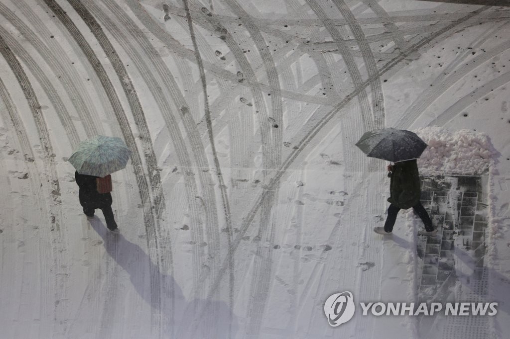 雪が降る中、傘を差して歩く市民＝２１日、ソウル（聯合ニュース）