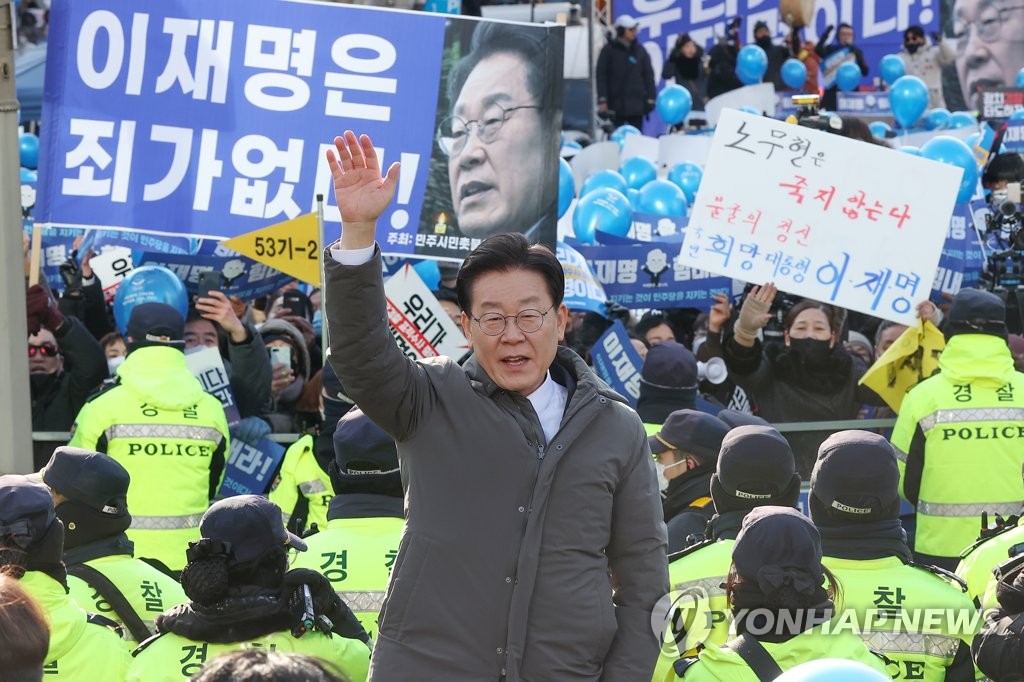 Los partidarios de Lee Jae-myung (centro), líder del principal partido opositor, el Partido Democrático, sostienen una pancarta que dice: "Lee Jae-myung no es culpable", mientras este los saluda con la mano antes de entrar en la Oficina de la Fiscalía del Distrito Central de Seúl, el 28 de enero de 2023, para someterse a un interrogatorio en relación con un proyecto de desarrollo inmobiliario, repleto de corrupción, en la ciudad de Seongnam, al sur de Seúl, que se propugnó cuando Lee era alcalde.