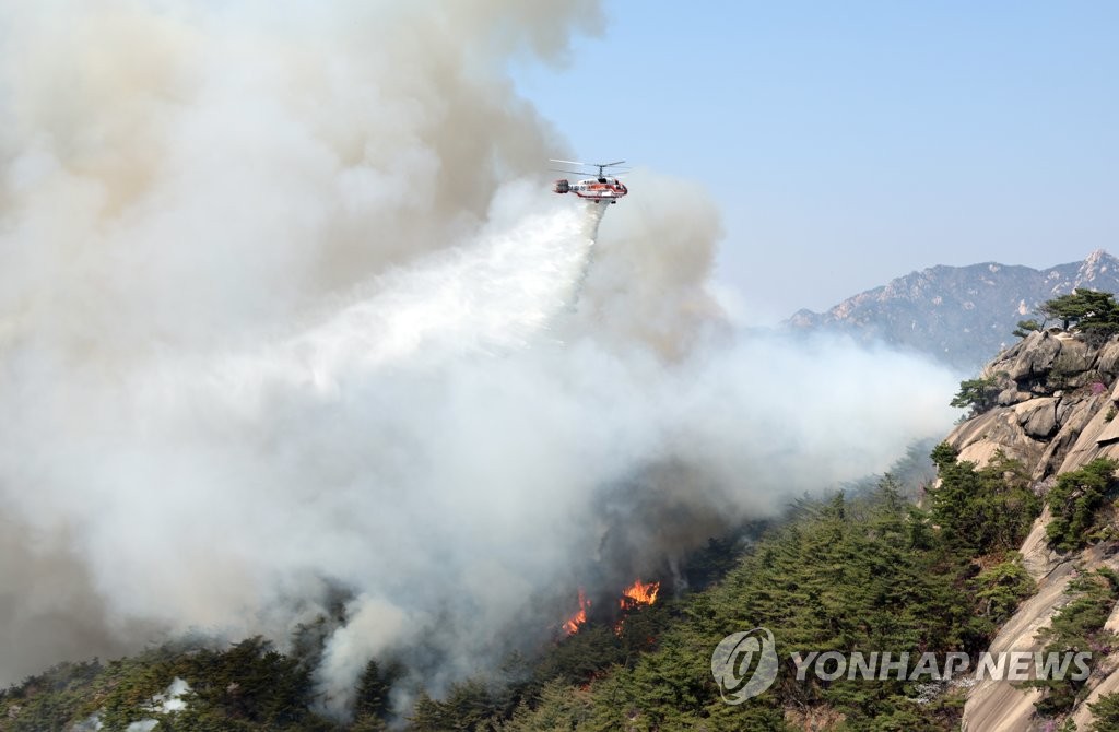A National Fire Agency helicopter dumps water to contain a fire at Mount Inwang in central Seoul on April 2, 2023. (Yonhap)